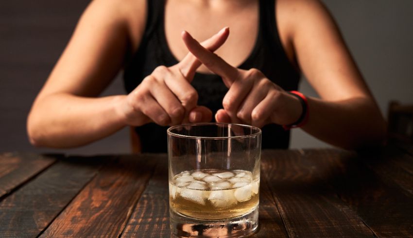 A woman is making a sign with her hands in front of a glass of whiskey.