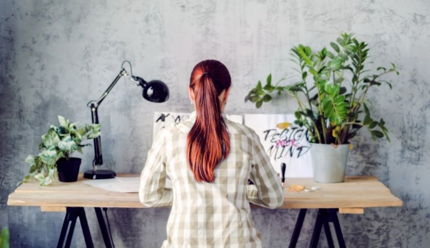 A woman sitting at a desk with a potted plant in front of her.