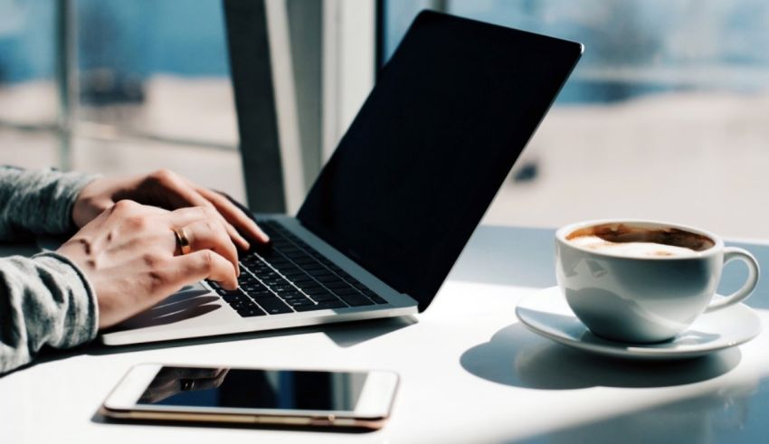 A person typing on a laptop with a cup of coffee.