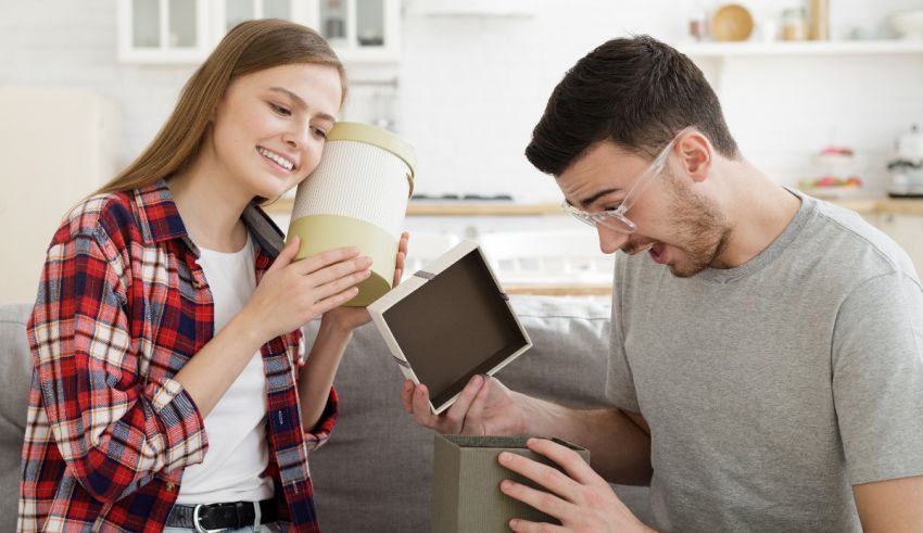 A man and woman are sitting on a couch looking at a gift box.