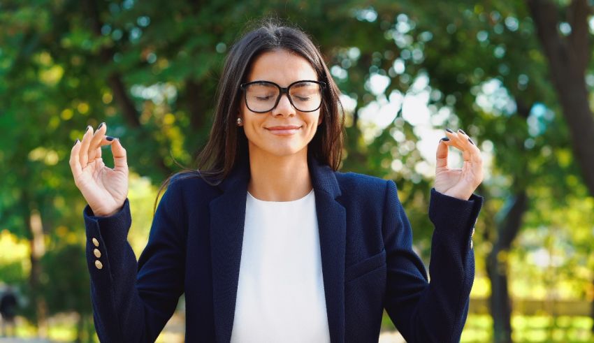 A woman in glasses is meditating in a park.