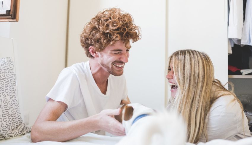 A man and a woman laughing while sitting on a bed.