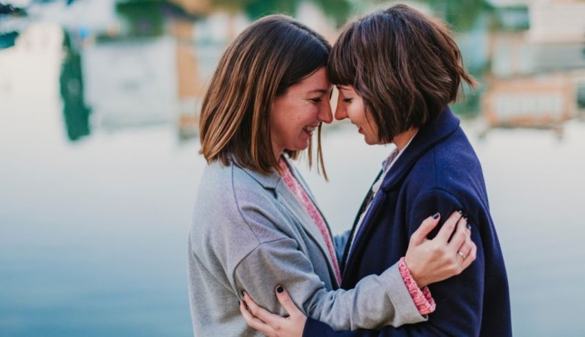 Two women hugging in front of a lake.
