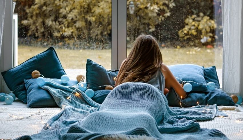 A woman in a blue blanket sitting on the floor in front of a window.