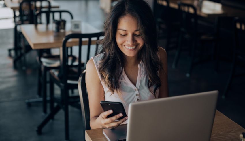 A woman sitting at a table with a laptop and cell phone.
