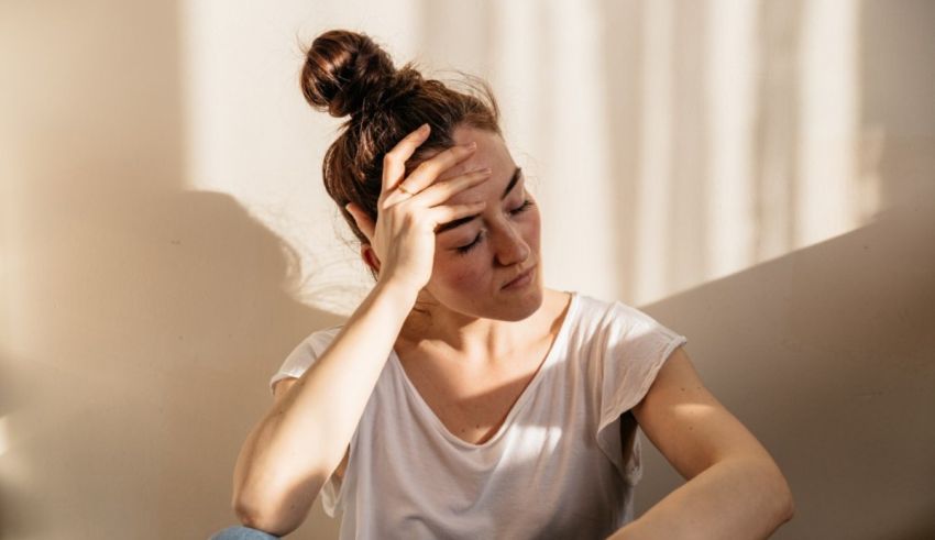 A woman is sitting on the floor with her hand on her head.