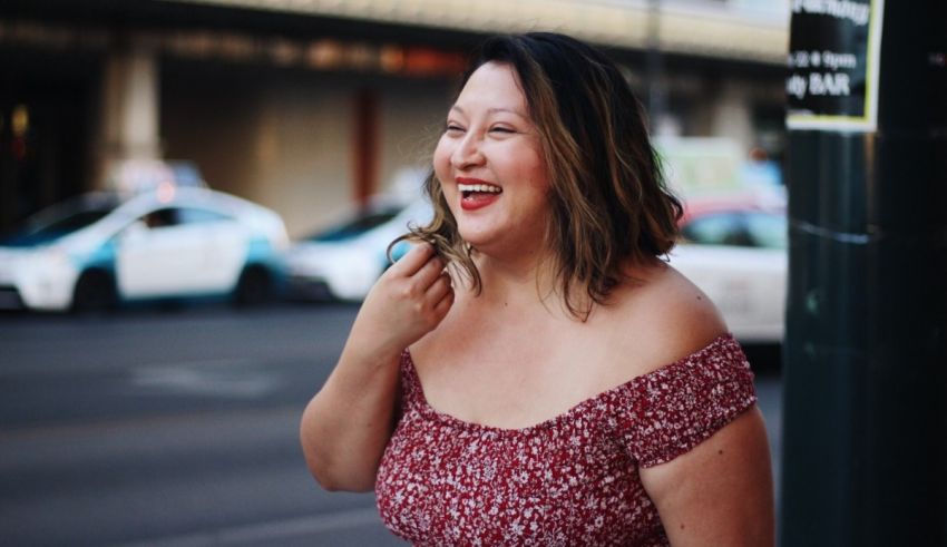 A woman laughing on the street in a red dress.