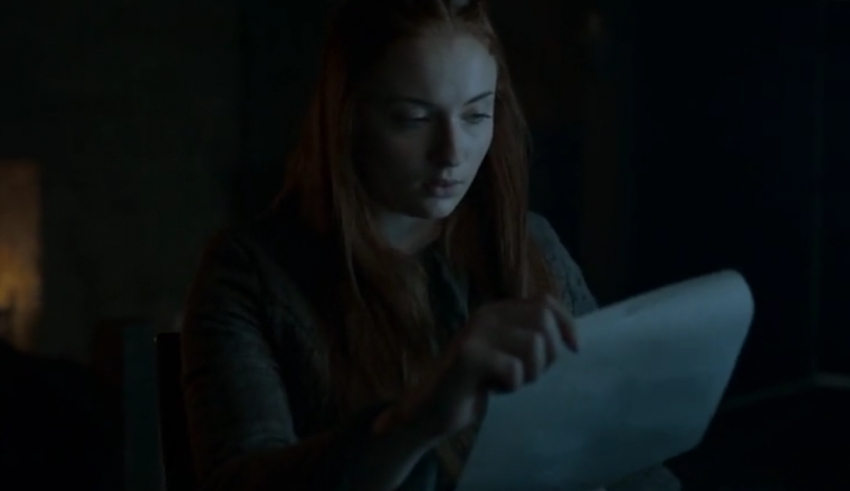 A woman is reading a paper in a dark room.