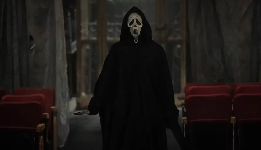 A man in a black hooded robe is standing in an auditorium.